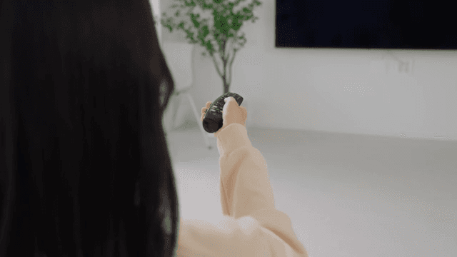 Woman operating television with remote control in bright living room