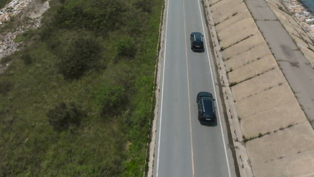Cars driving on a coastal road surrounded by greenery and the sea