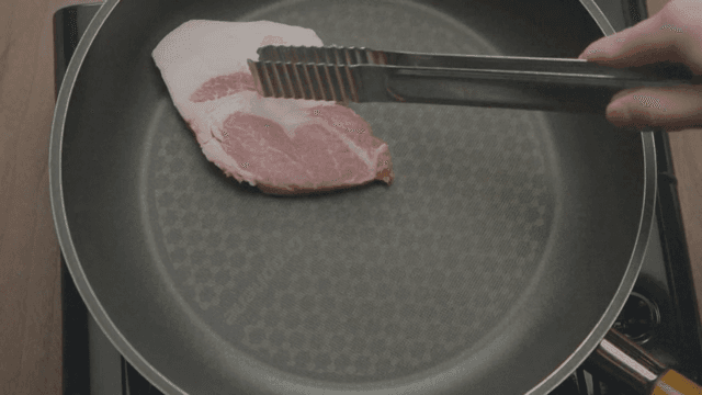 Raw pork slices being placed in a pan