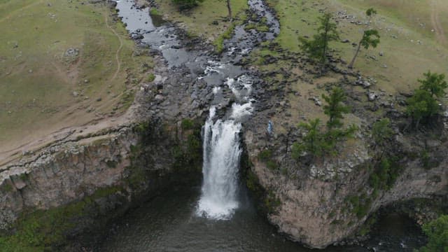 Aerial View of a Stream and Waterfall Flowing Through Grasslands