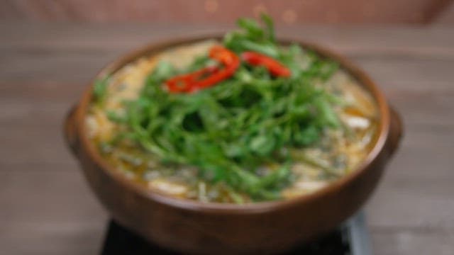 Steaming soup dish adorned with fresh water parsley and red chili