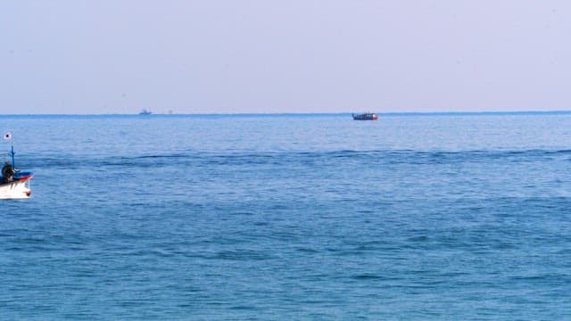 Fishing boats traveling across calm sea under clear sky