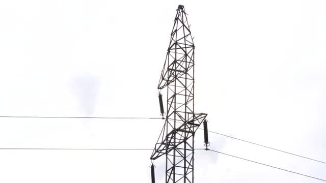 Tall power line tower in front of a factory with smoke