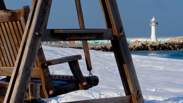 Wooden swing in the snowy beach with a lighthouse in the distance