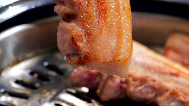 Grilled pork belly being cut with scissors