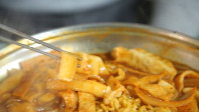 Chopstickful of rice cake in tteokbokki with ramen