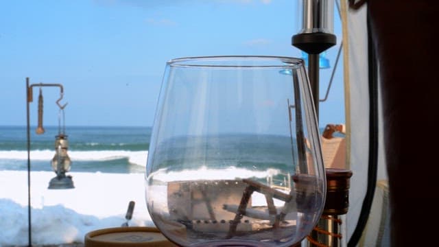 Pouring wine into a glass inside a tent facing the ocean