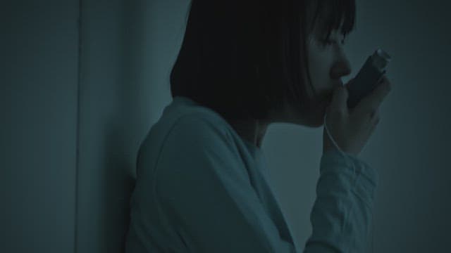 Woman breathing through an inhaler for asthma in a dark room