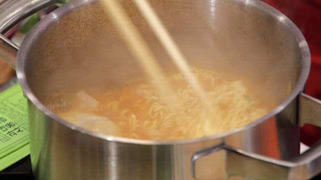 Stirring ramyeon in a pot with chopsticks