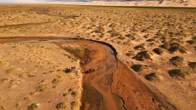 People riding camels crossing a desert river