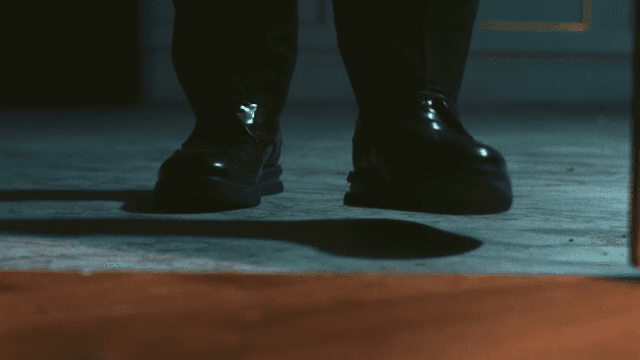 Man in formal shoes appears behind the wooden door