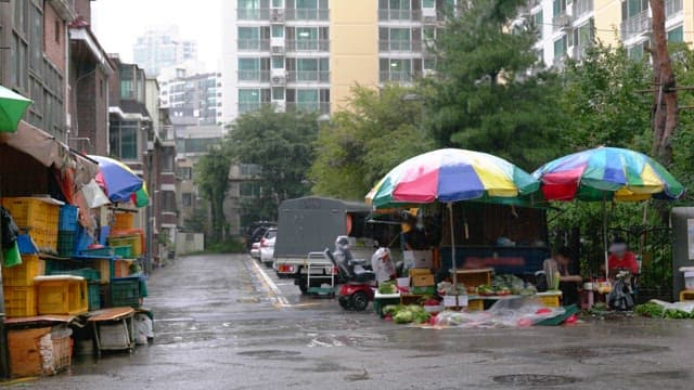 Vendors selling vegetables in an alley next to an apartment complex