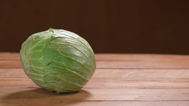 Hand placing fresh cabbage on wooden table