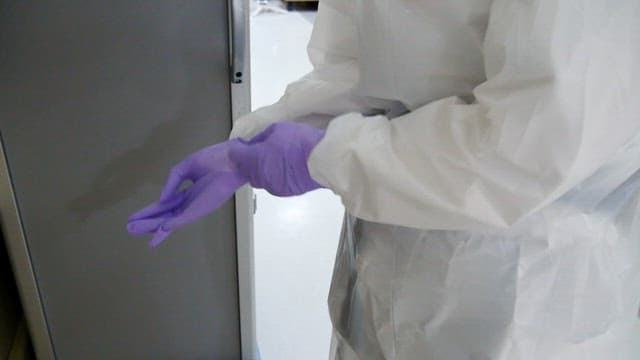 Person in a protective suit weaing purple gloves in a medical facility