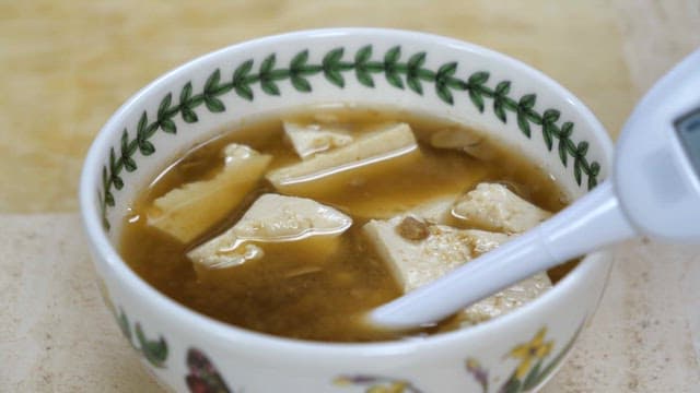 Hands testing soybean paste soup salinity with a salinity meter indoors