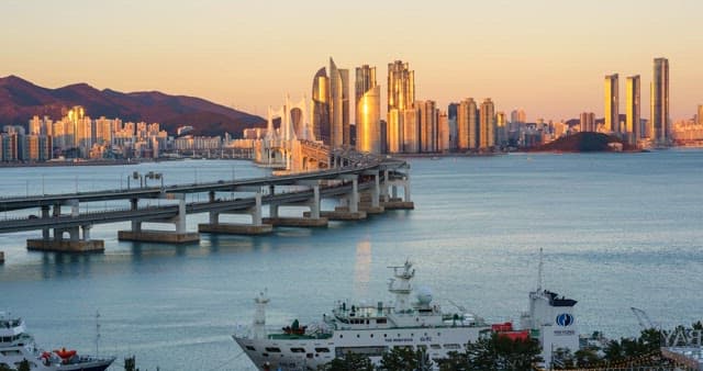 From evening to night view of a bustling port city Busan with tall skyscrapers and Gwangan Bridge