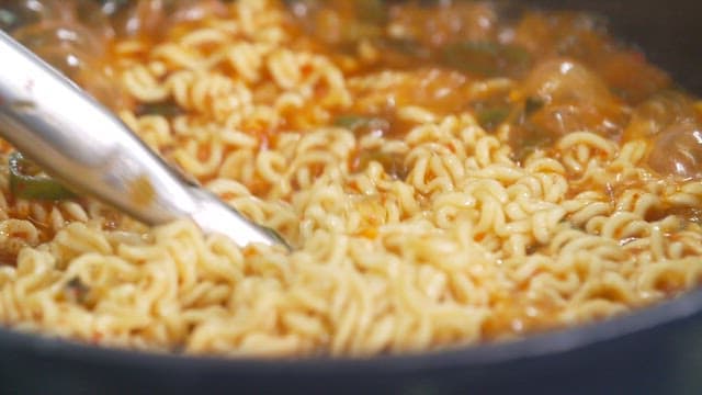 Delicious ramen boiling in a pot with tongs