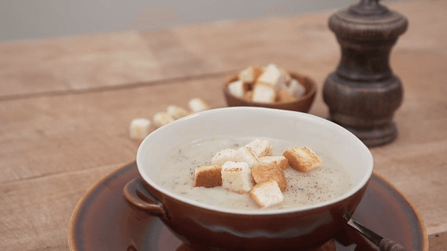 Bowl of button mushroom soup topped with toasted bread crust