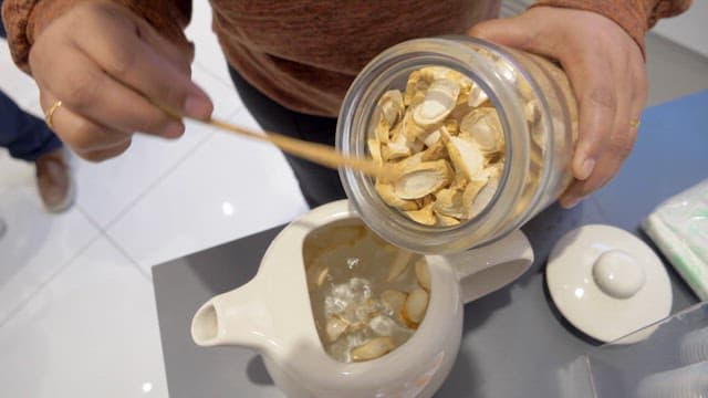 Putting dried ginseng pieces into a teapot to make tea