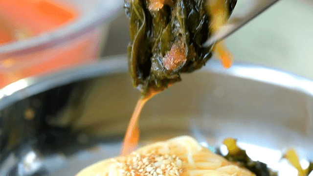 Adding yeolmu kimchi to cold noodles in a bowl