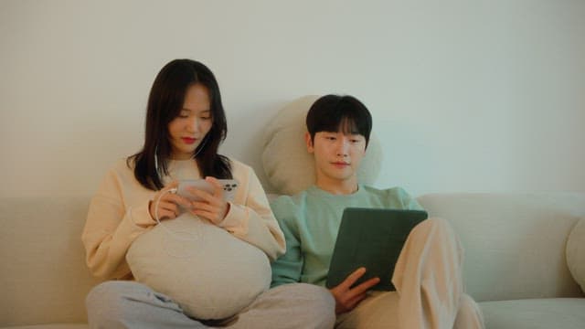 Two people using digital devices on a sofa in cozy living room