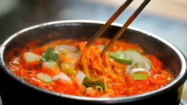 Stirring spicy seafood ramyeon with chopsticks
