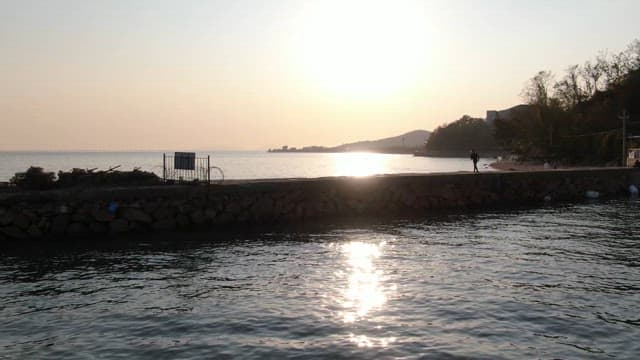 Person jogging on a breakwater with the peaceful sea at dusk