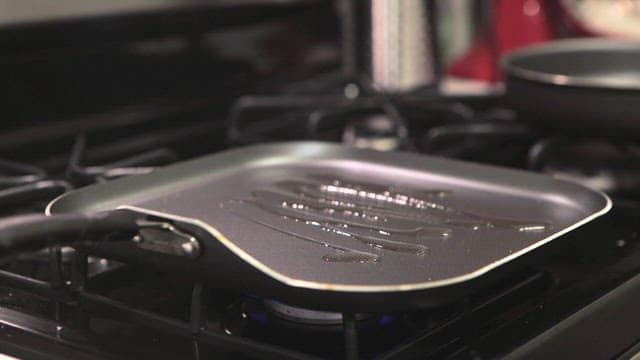 A person preparing a burger patty on a preheated oiled pan indoors