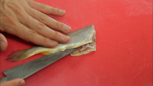 A person filleting a fish on a red cutting board