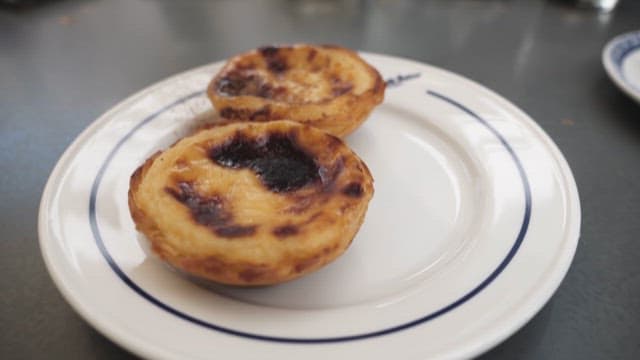 Sprinkling Cinnamon on Two Egg Tarts on a White Plate