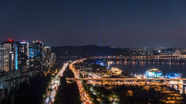 Bustling cityscape at night with lit skyscrapers and lively traffic near a river