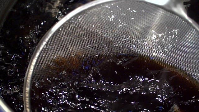 Bay leaves being strained from black sauce