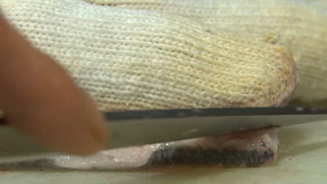 Sliced raw scaled sardine being prepared on a cutting board in a sushi restaurant kitchen