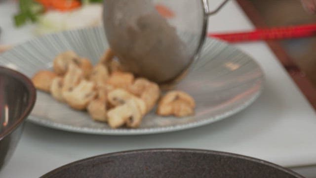 Putting fried button mushrooms on a plate with a sieve