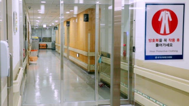 Empty hospital corridor with sign requiring protective clothing