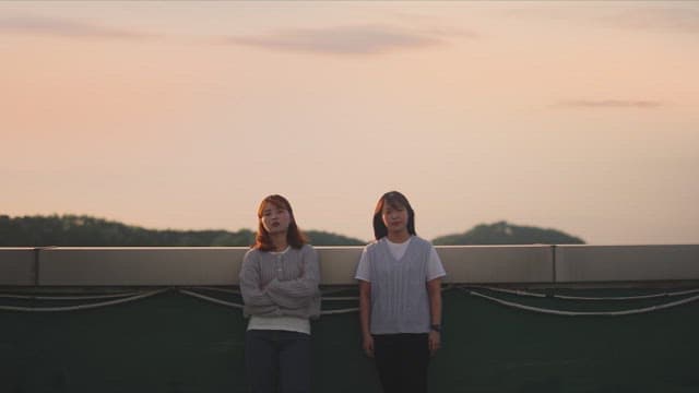 Two women on a rooftop with their backs to the sunset sky