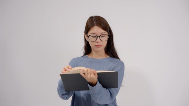 Long haired woman wearing glasses reading a book in a quiet room