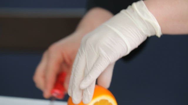 Gloved hand slicing an orange on a cutting board