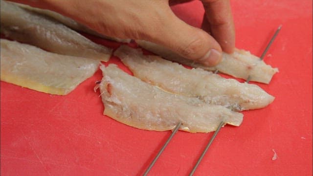 Hand preparing fish fillets on skewers
