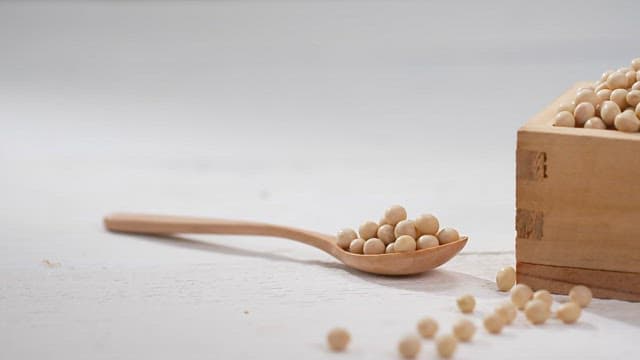 Wooden spoon and a wooden box with soybeans on a white surface