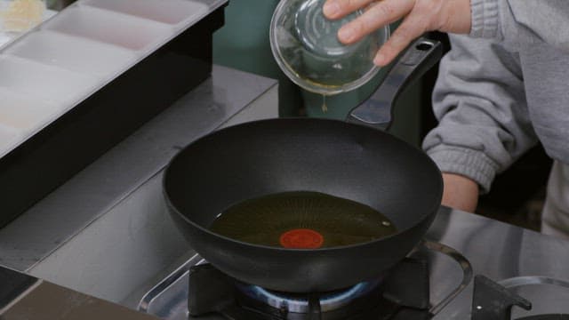 Pouring oil into a heated frying pan in a modern kitchen