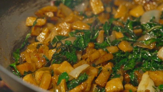 Sautéing spinach and tuna in a frying pan over an outdoor fire