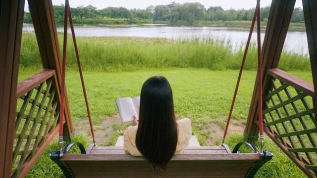 Woman Reading on Swing Overlooking Lake