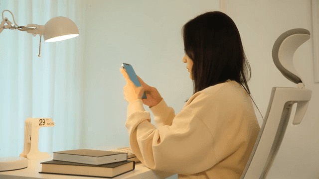 Woman using a smartphone at a desk in a calmly lit room