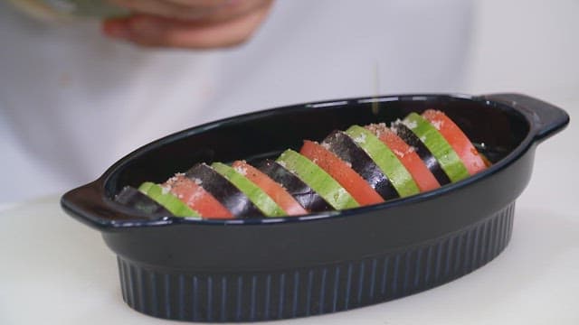 Drizzling olive oil on atatouille with zucchini and tomatoes