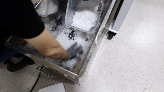 Worker scooping and transferring plastic pellets in a factory