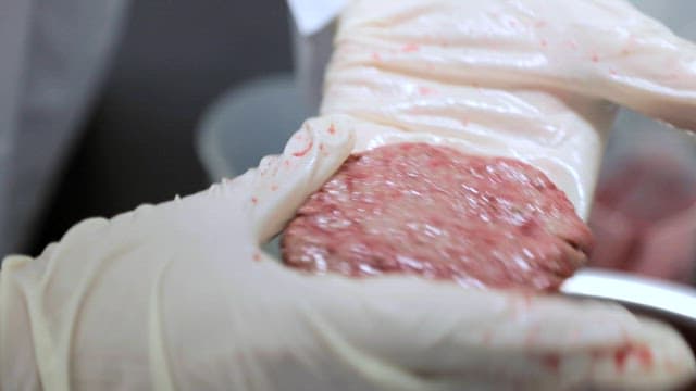 Gloved hand assembles a meat patty