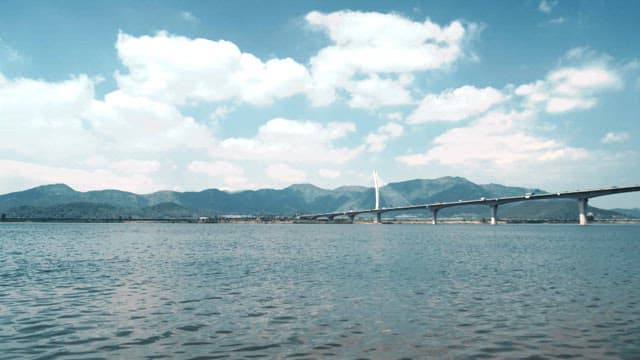 Bridge with cars passing over a calm sea and distant mountains