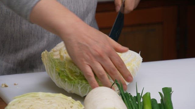 Person slicing a fresh cabbage with a knife on a cutting board