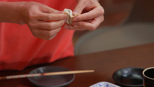 Person wearing a red shirt making dumplings at a wooden table